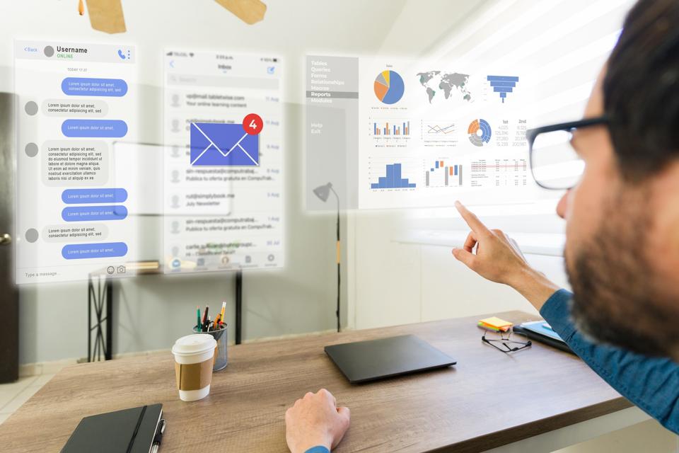 A man wearing AR glasses pointing at holographic screen with data, charts and emails.