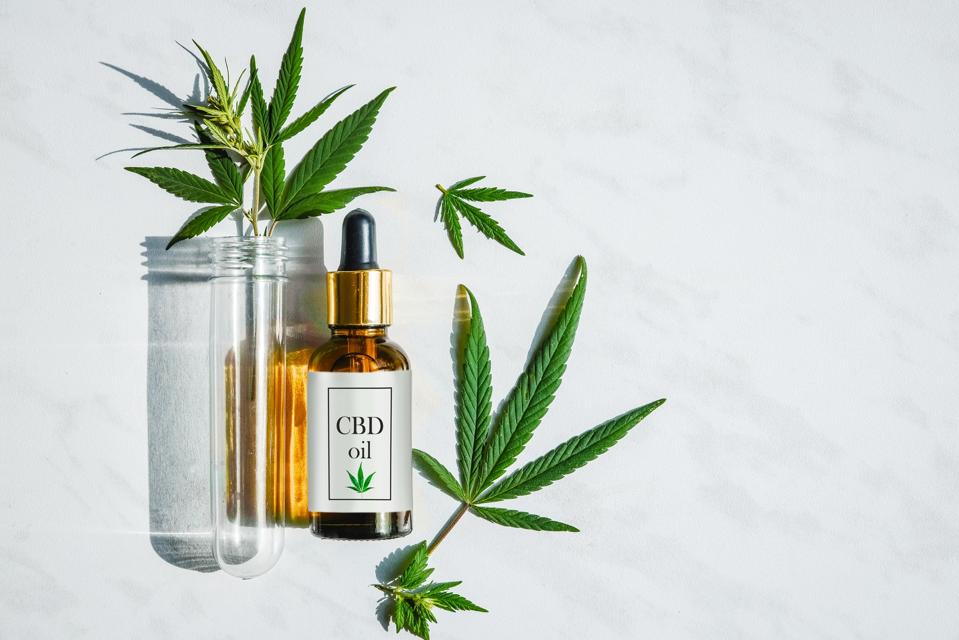 Glass bottle with cannabis oil with label and a test tube with hemp leaves on a marble background. Copy space.