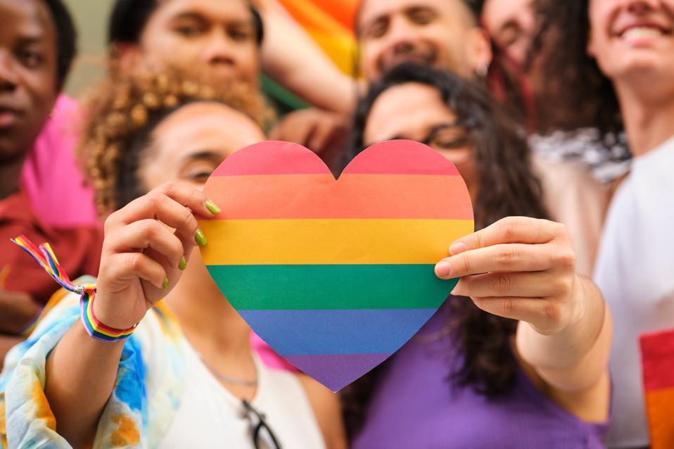 A group of LGBTQ people holding a rainbow heart celebrating Pride Month.