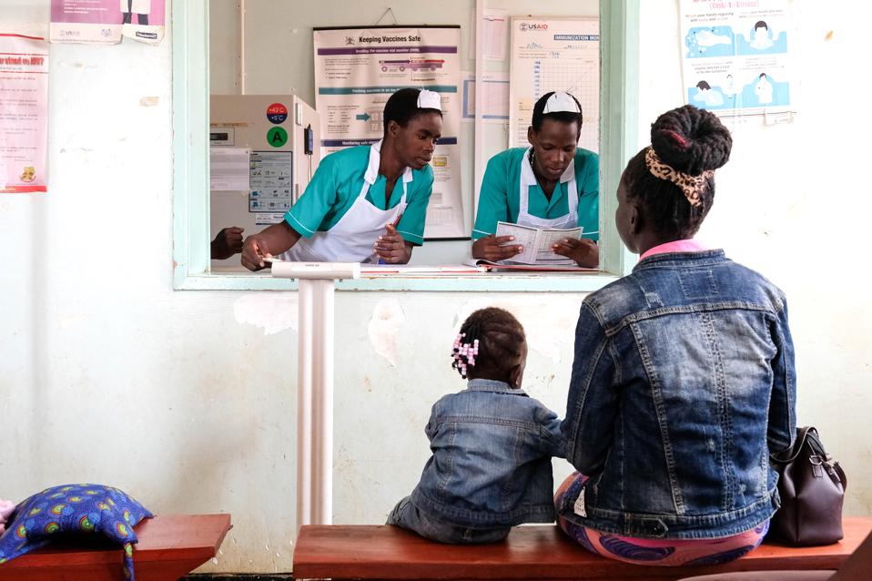 A mother and daughter dressed identically sit on a bench in front of a clinic window