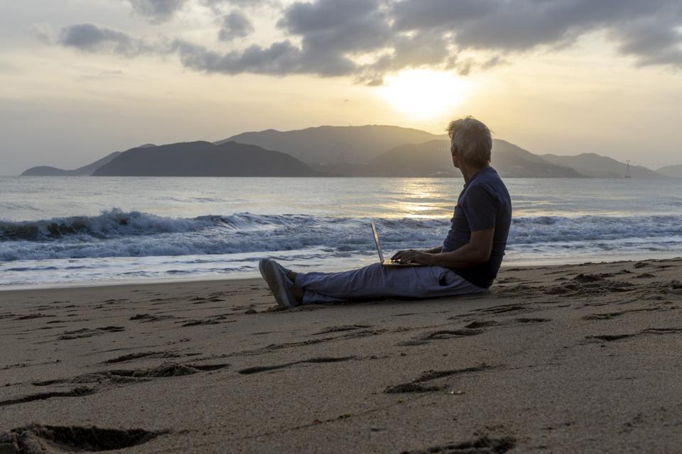 Older male working on laptop on beach at sunrise