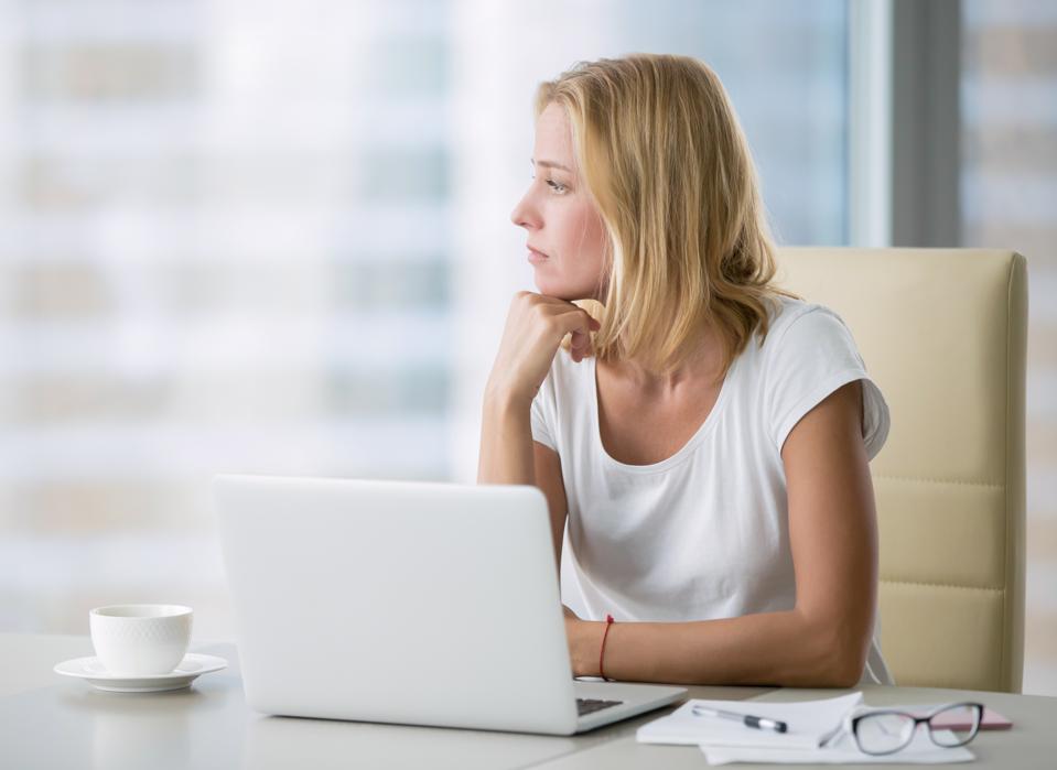 Female professional looking out the window while working on a laptop, reflecting on how to stay focused at work during uncertain times.