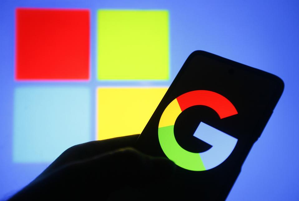 Google logo on smartphone, Microsoft logo behind.