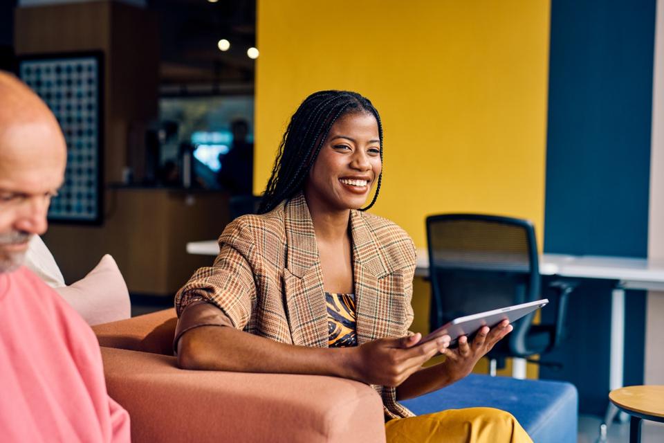 Smiling African American businesswoman in a plaid blazer holding a tablet in a modern office. Empowerment and professional growth in business concept