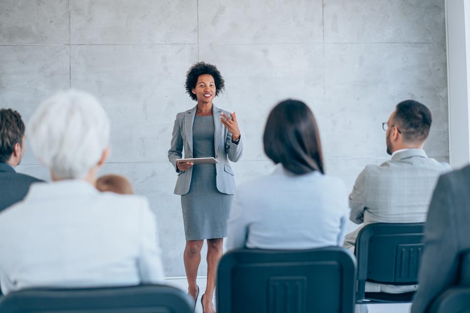Happy business leader talking to group of her colleagues on a seminar in a meeting room.