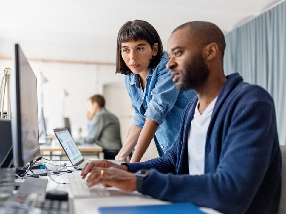Two businesspeople looking at desktop computer monitor and discussing work at desk