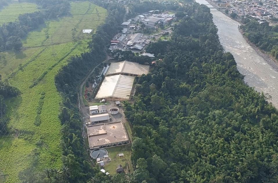 An aerial view of a river, forest, structures, and fields along each other