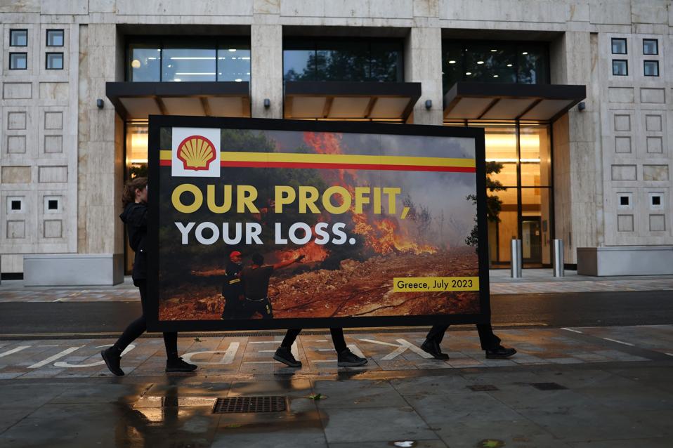 Three people carry a billboard that reads "Our profit, your loss," showing the Shell logo