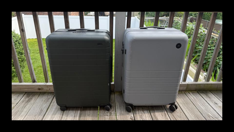A green Away The Medium suitcase next to a grey Monos Medium Check-In suitcase.