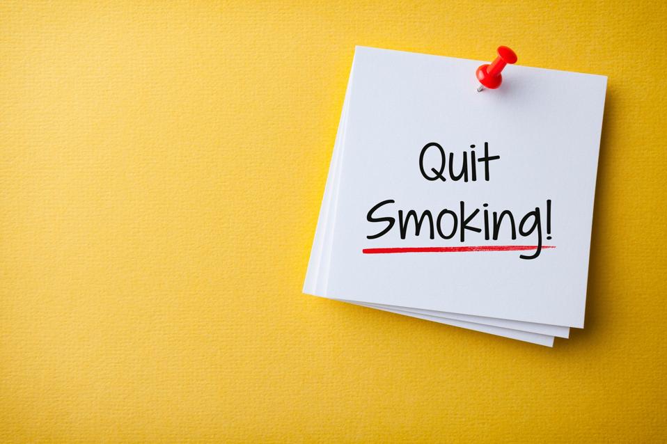 White Sticky Note With Quit Smoking And Red Push Pin On Yellow Cardboard Background
