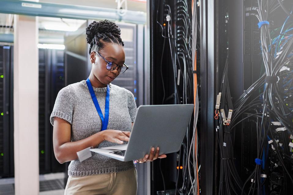 Shot of a young woman using a laptop in a server room