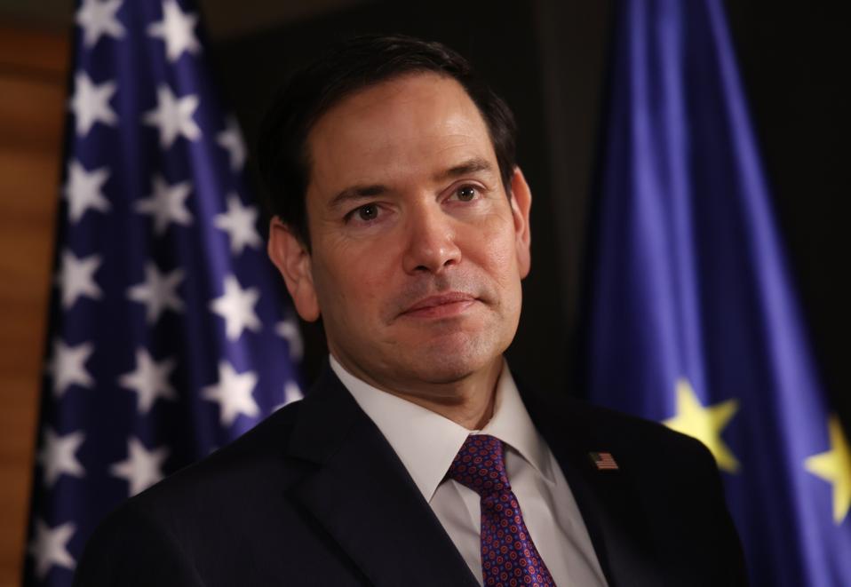 U.S. Secretary of State Marco Rubio stands in front of an American flag