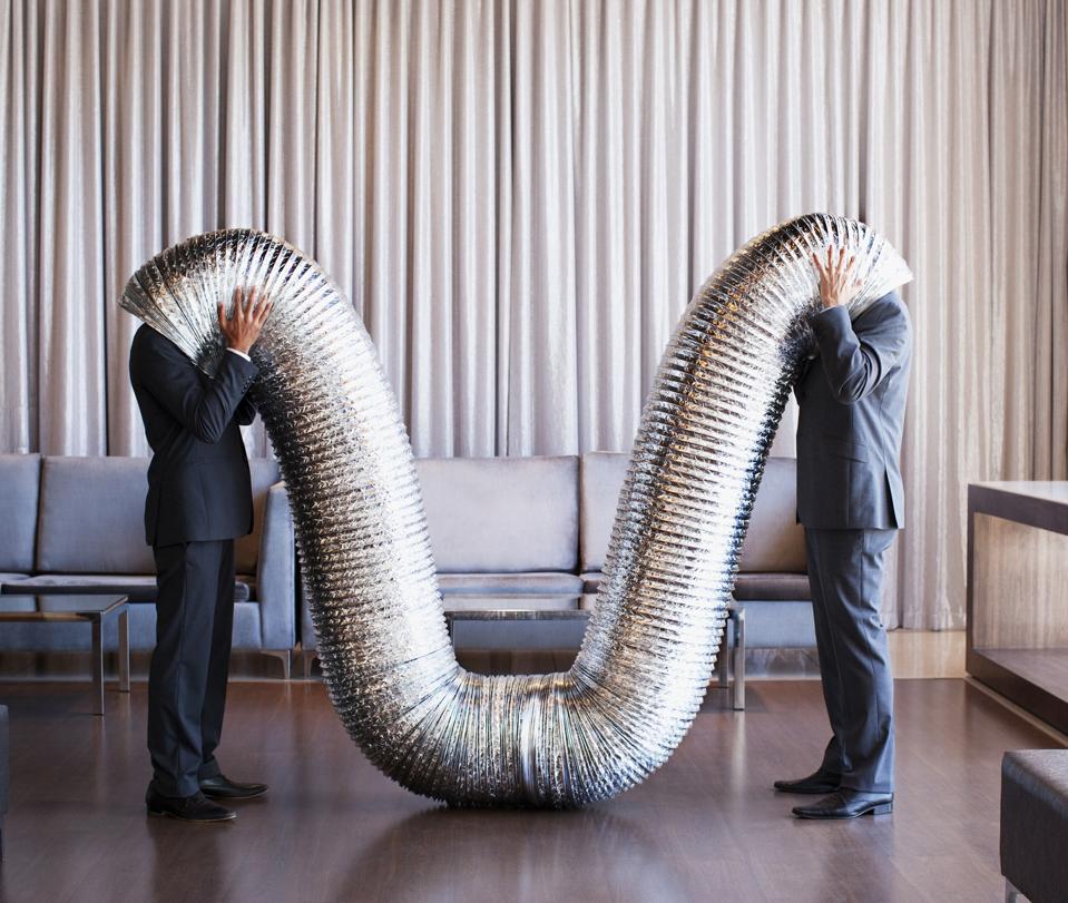 Businessmen with their heads inside metal tubing