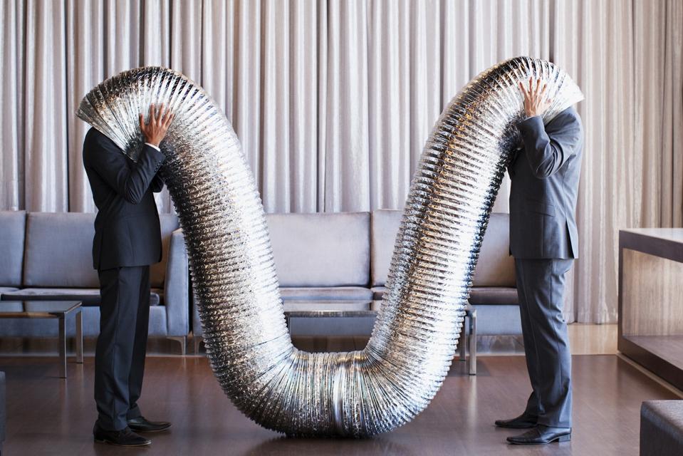 Businessmen with their heads inside metal tubing
