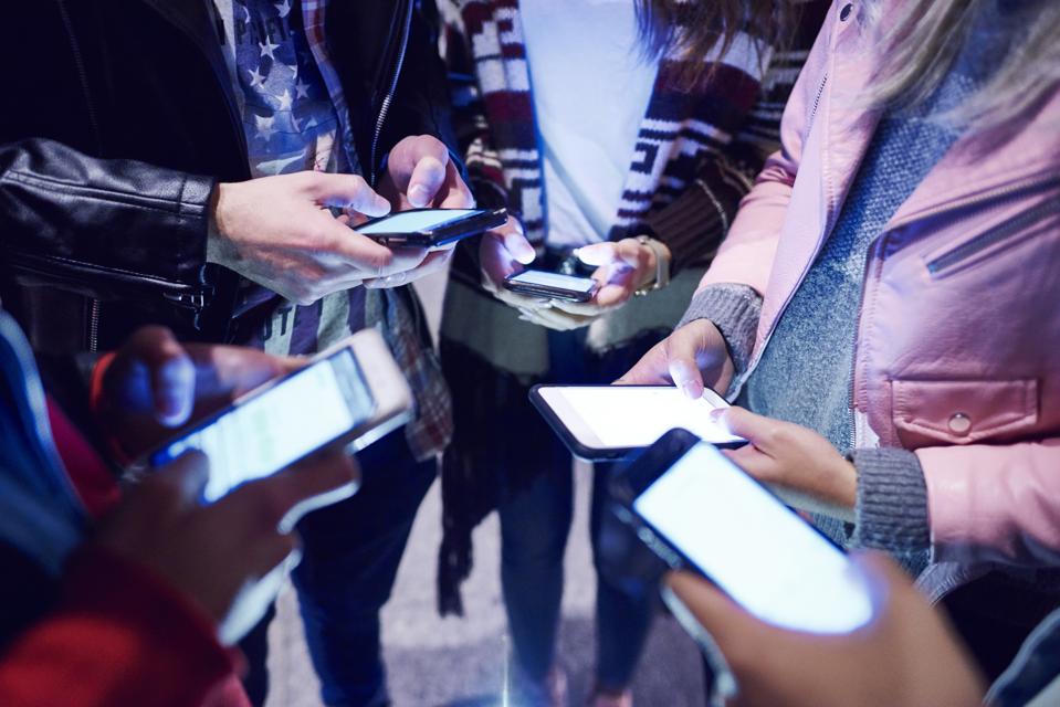 Mid section of young adult friends standing in circle looking at smartphones