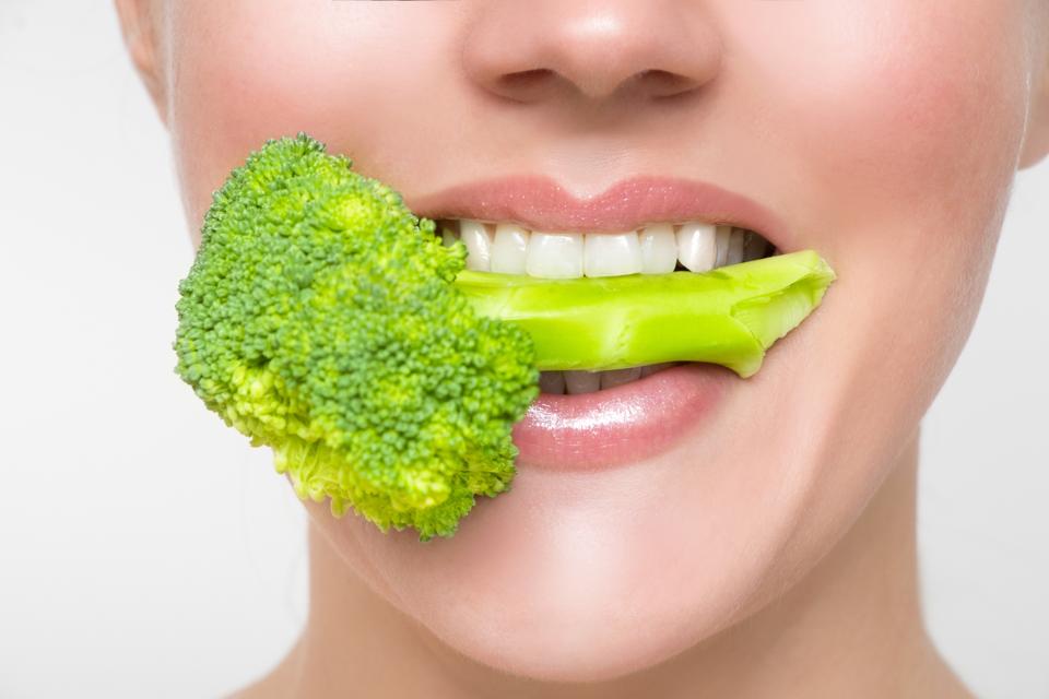 Hermosa mujer se ríe con un trozo de brócoli entre sus grandes dientes