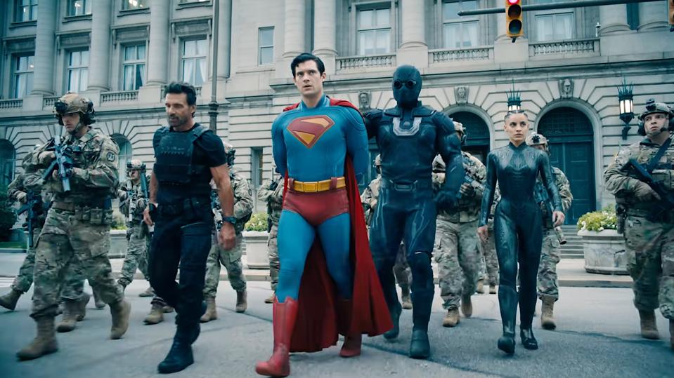 Superman being escorted by a masked person and armed guards