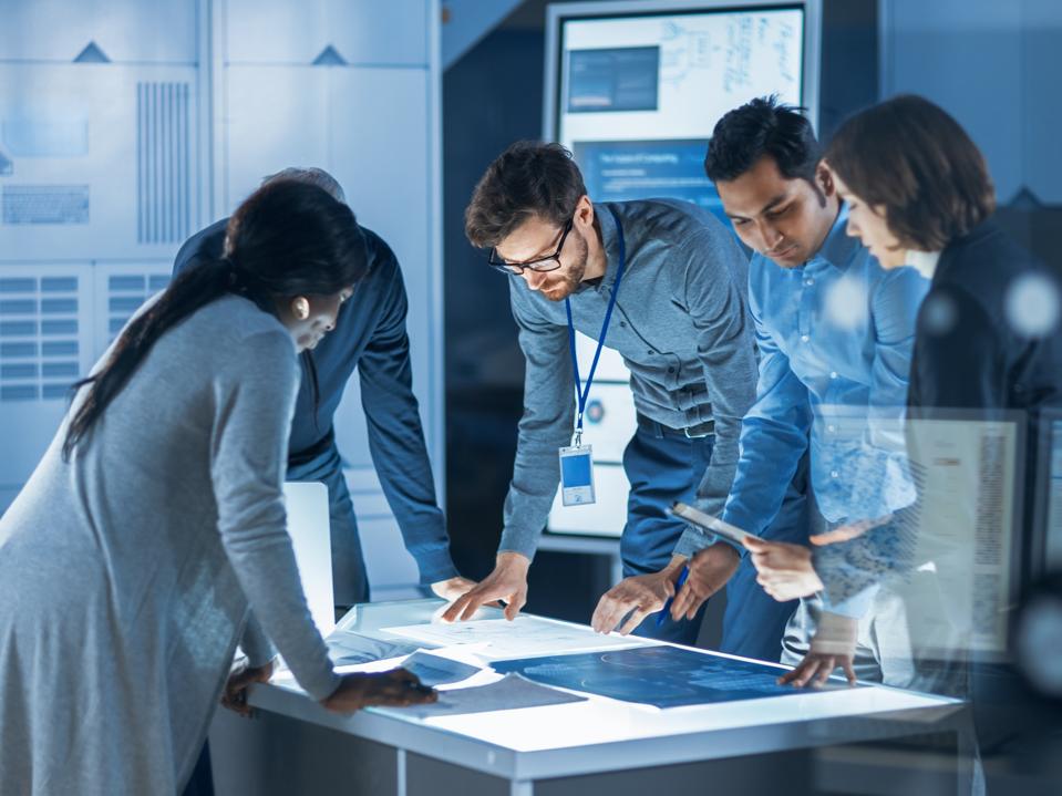 Engineers Meeting in Technology Research Laboratory: Engineers, Scientists and Developers Gathered Around Illuminated Conference Table, Talking and Finding Solution. Industrial Design Facility