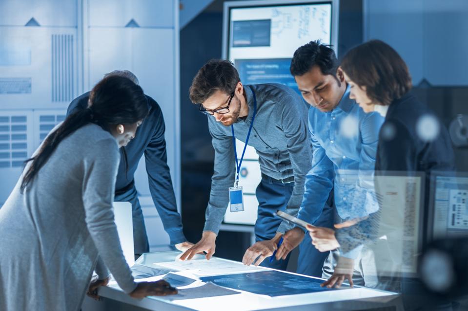 Engineers Meeting in Technology Research Laboratory: Engineers, Scientists and Developers Gathered Around Illuminated Conference Table, Talking and Finding Solution. Industrial Design Facility
