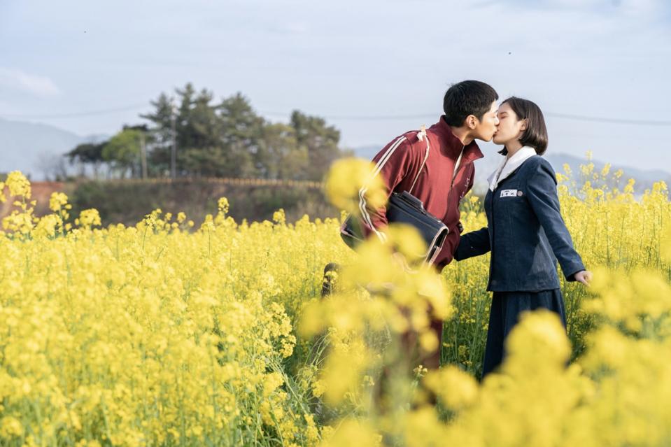 A man kisses a woman in a flowery field.