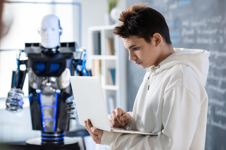 A student preparing a presentation with a robot in the classroom.