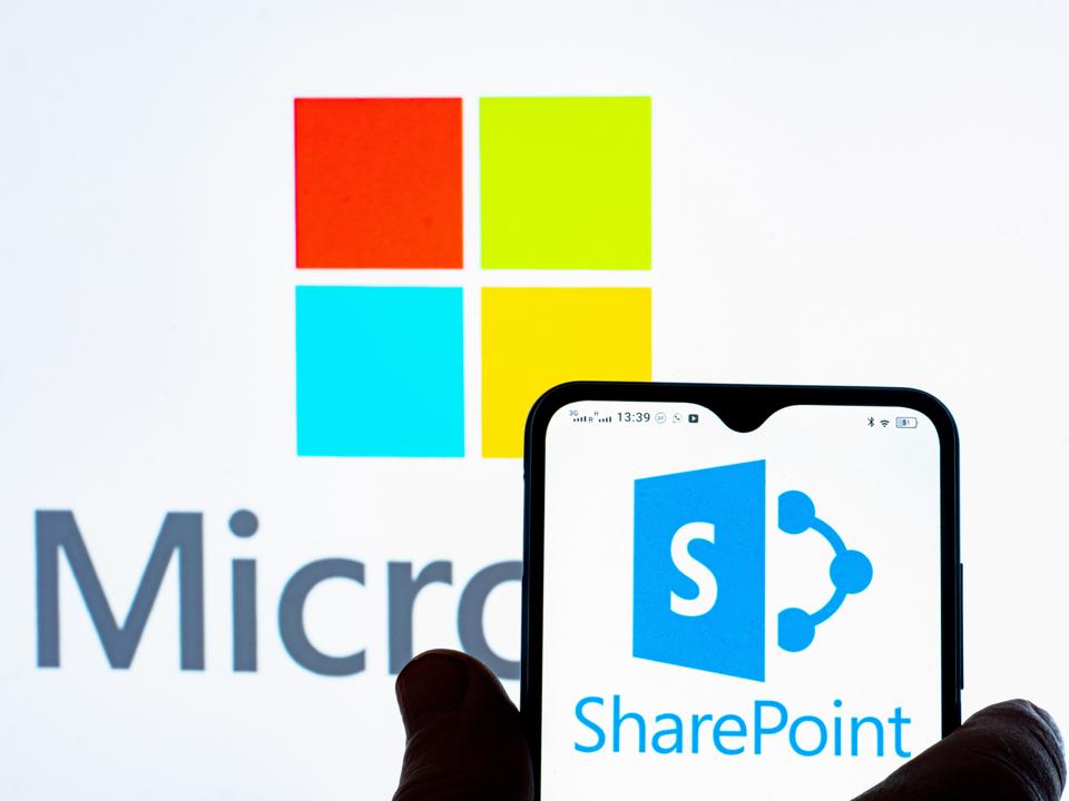Microsoft SharePoint logo is seen displayed on a smartphone and Microsoft logo in the background.