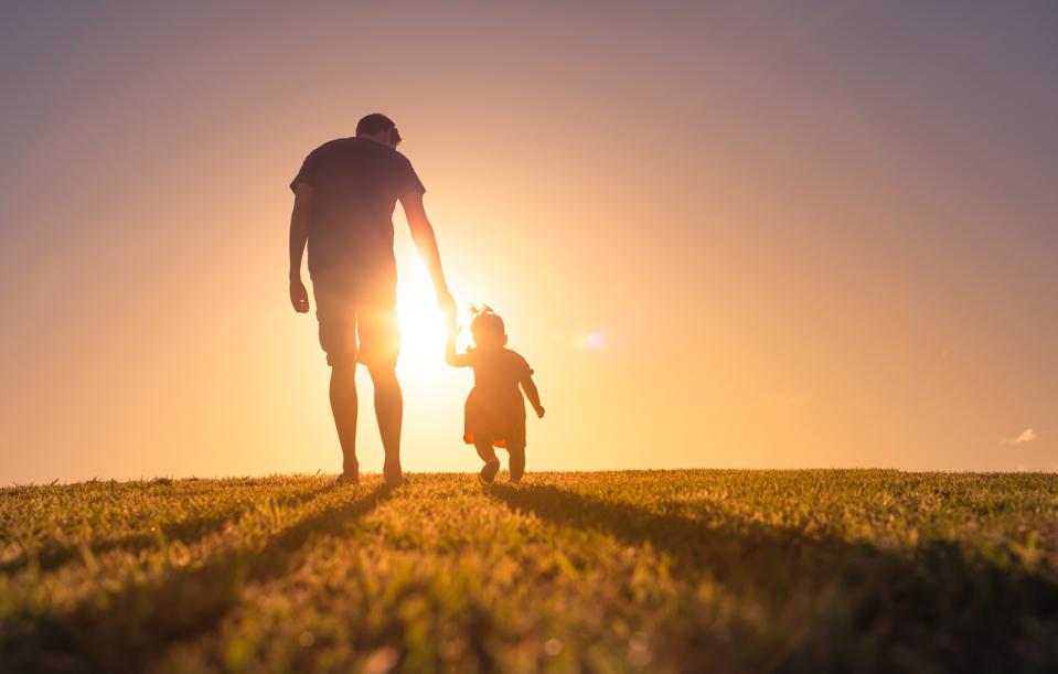 Father and daughter holding hands and walking at sunset outdoors.