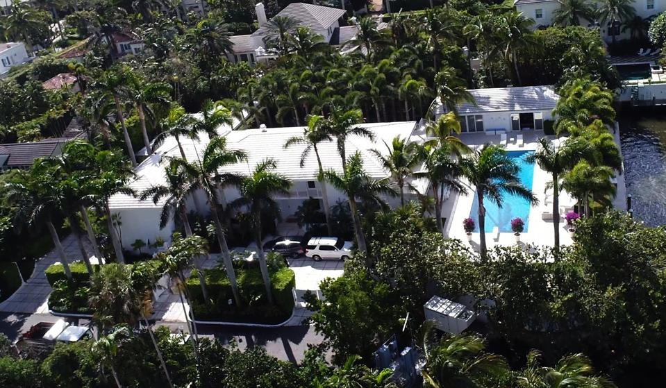 A white house with a pool on the right, framed by palm trees, in Palm Beach formerly owned by Jeffrey Epstein.