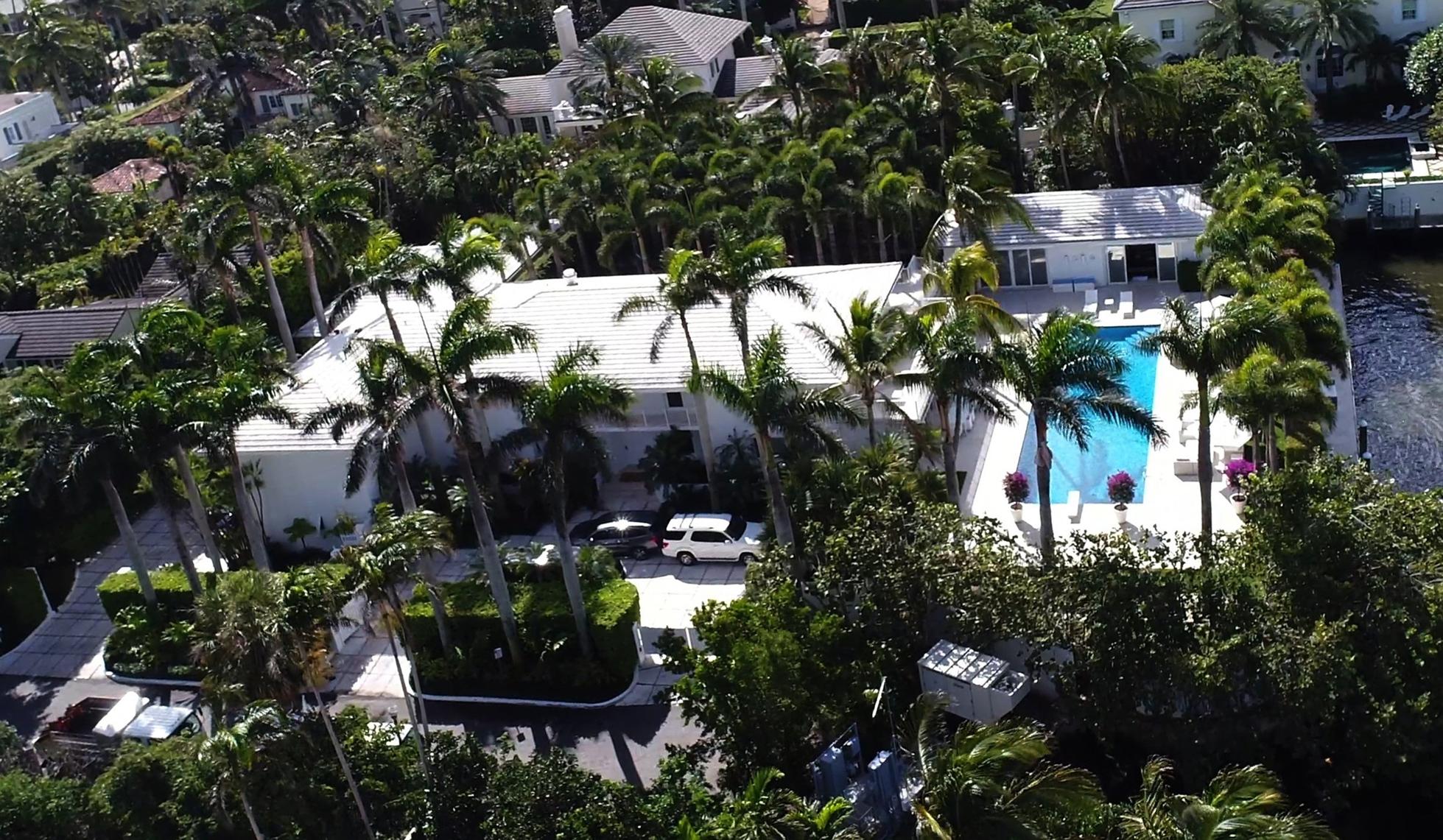 A white house with a pool on the right, framed by palm trees, in Palm Beach formerly owned by Jeffrey Epstein.