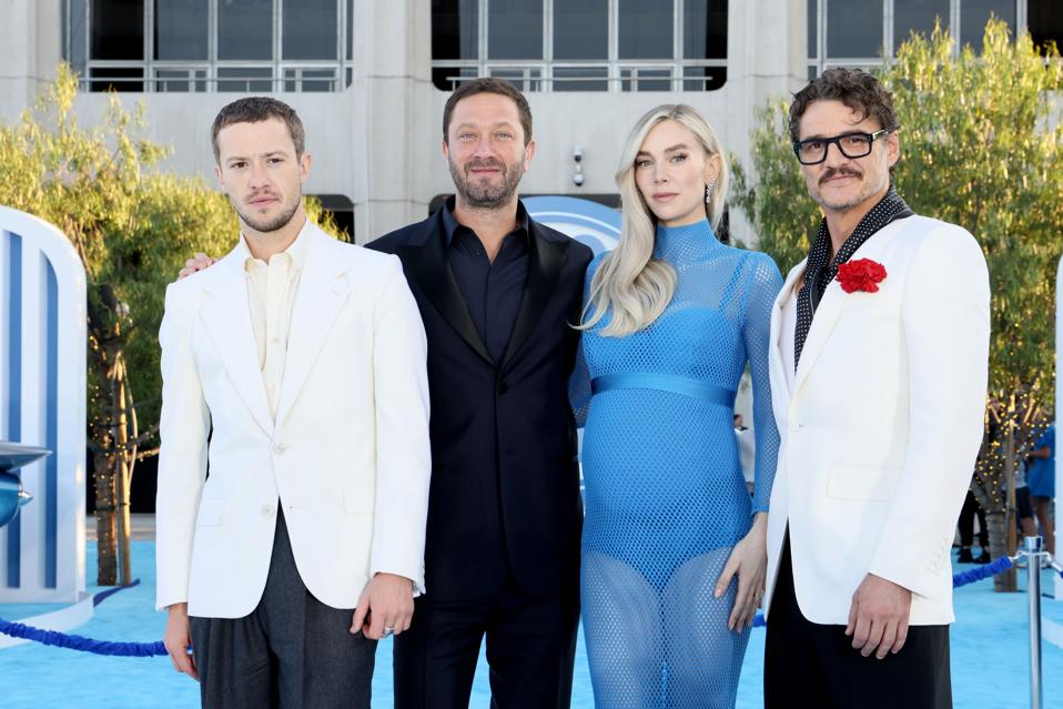 A man in a white suit, a man in a black suit, a woman in a blue dress and a man in a black and white suit