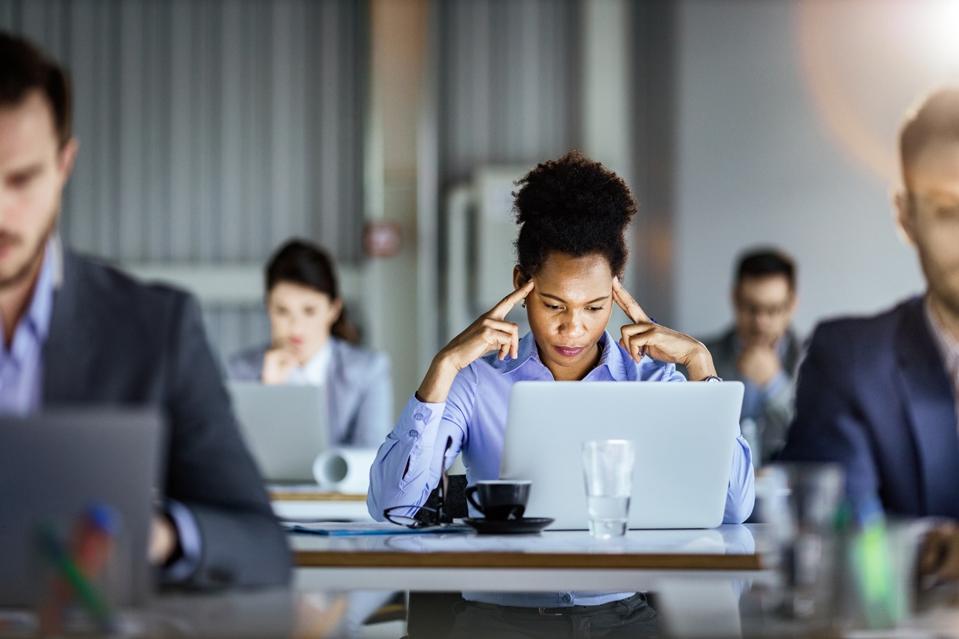 Thoughtful black businesswoman working on laptop in the office full of people.