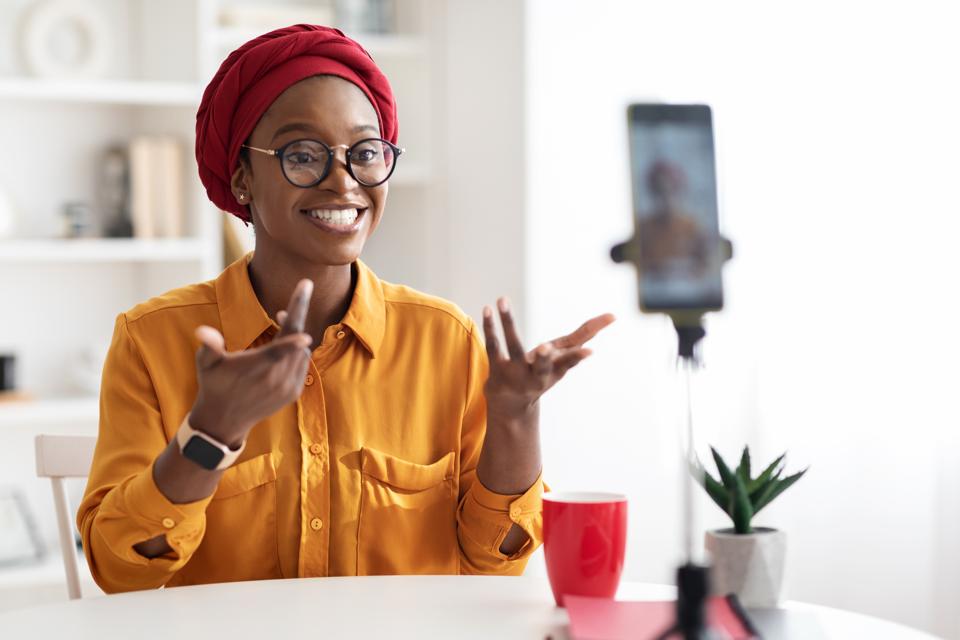 Cheerful stylish black lady blogger streaming from home