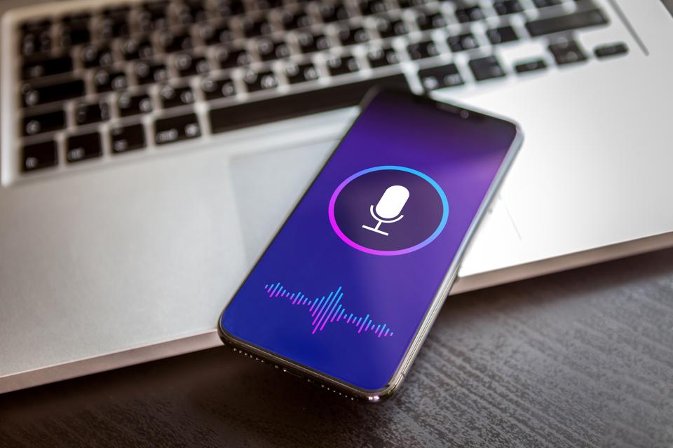 Smartphone with a voice assistant interface displayed on screen, resting on a laptop keyboard — symbolizing the shift from keyboard to voice AI.