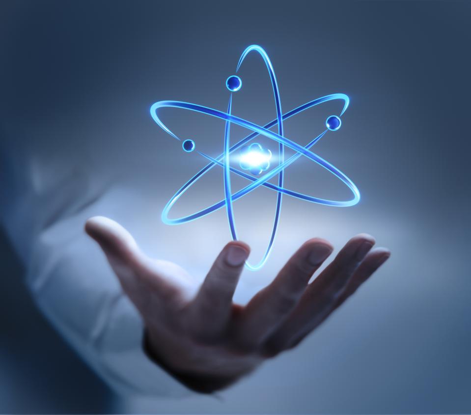Hand with atom nucleus and electrons symbol for the best nuclear stocks to buy now.