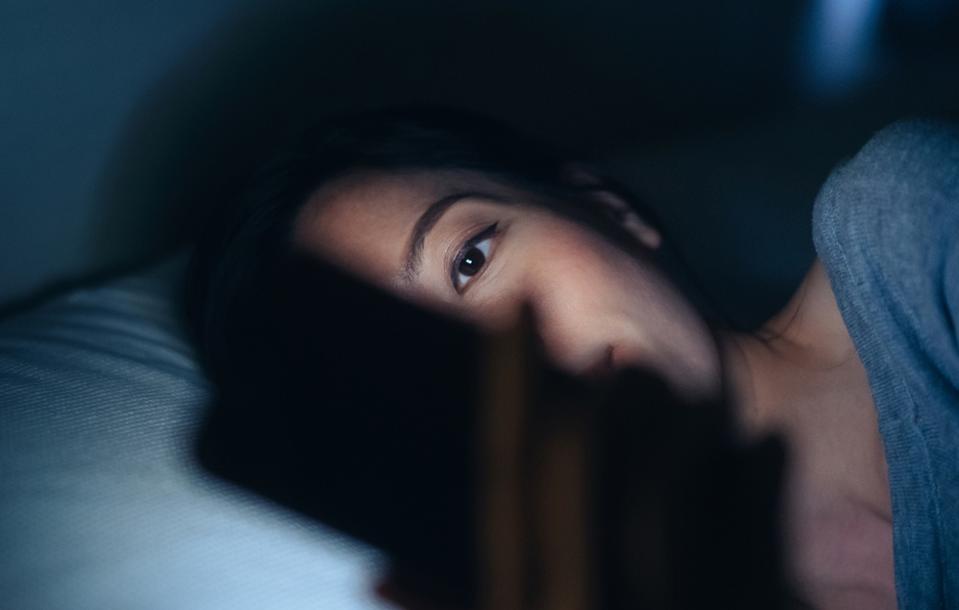 Young woman in bed using phone.