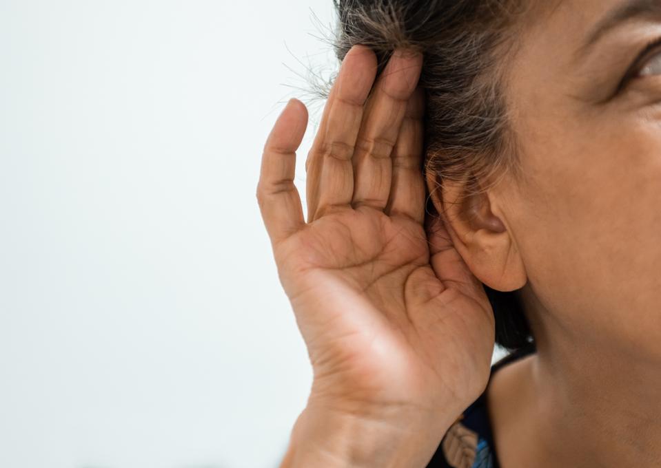 Woman cups hand to her ear to hear better