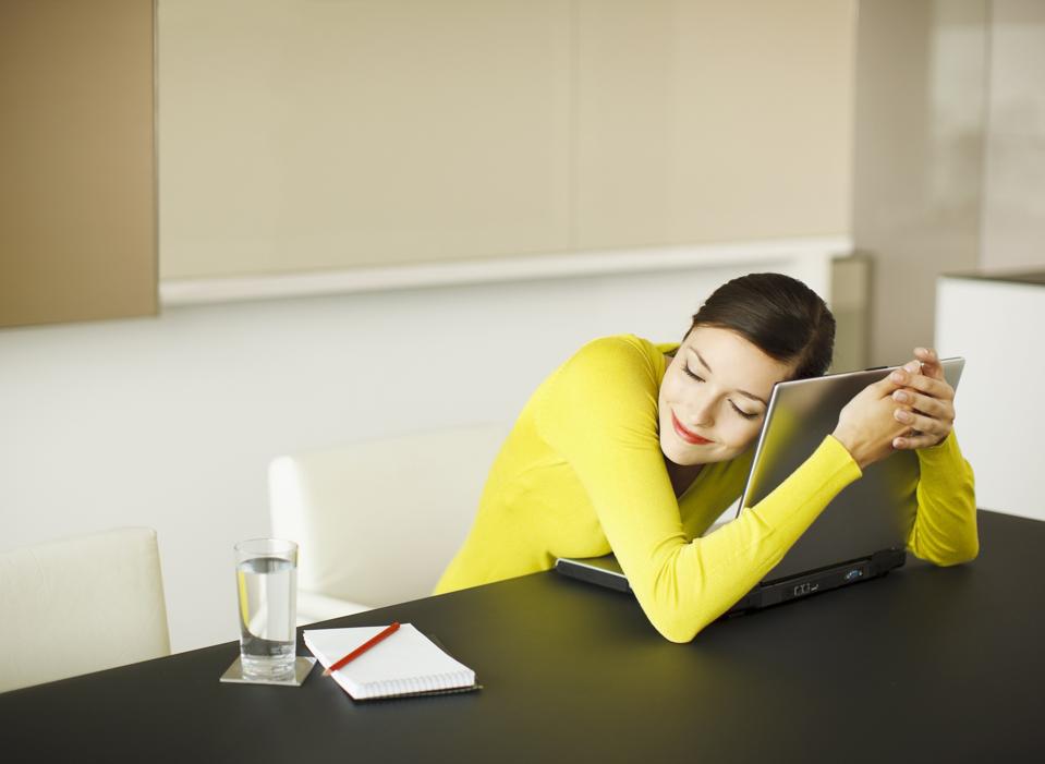 Smiling businesswoman hugging laptop in conference room