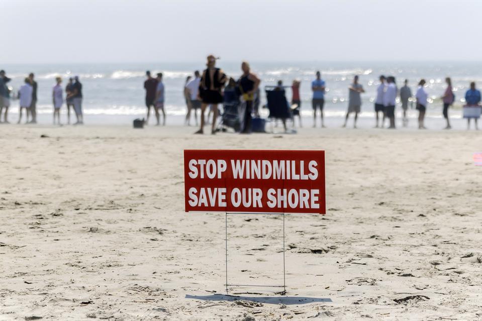 A red sign that reads Stop Windmills Save Our Shore installed on beach