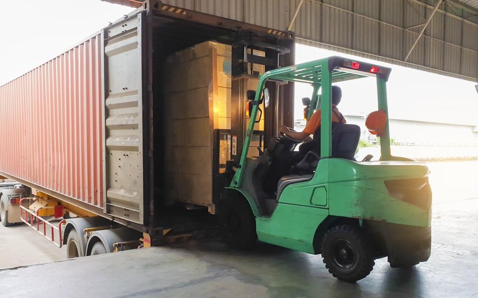 Forklift driver loading goods pallet into the truck container.
