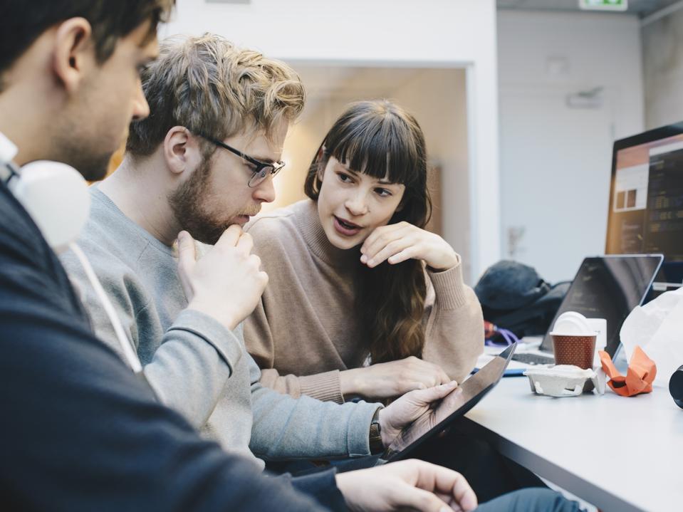 Male and female computer programmers discussing over digital tablet at desk in office