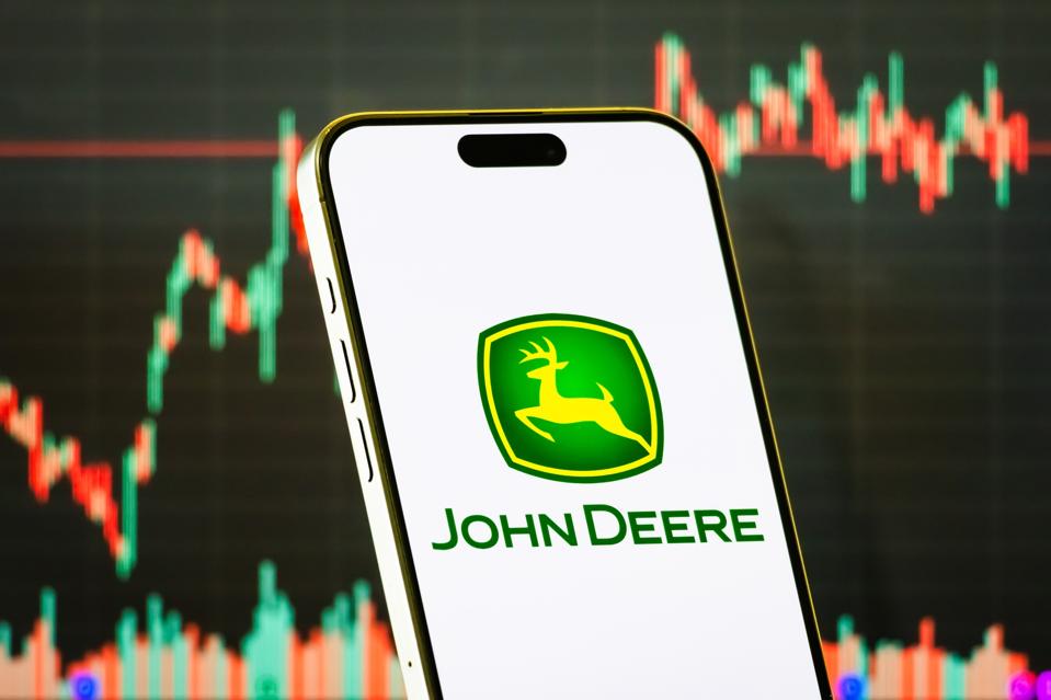 John Deere logo on smartphone with stock market chart in background