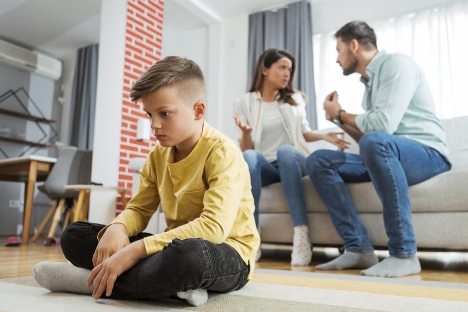 Sad boy listening to his parents fighting looking down