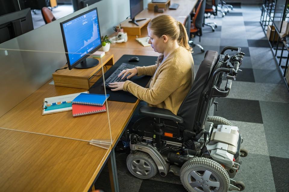 A businesswoman with a disability works diligently on her desktop PC in a modern office environment.