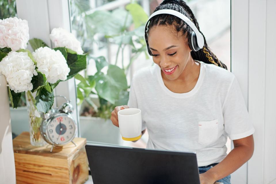 Black woman working remotely on laptop, smiling with coffee and headset