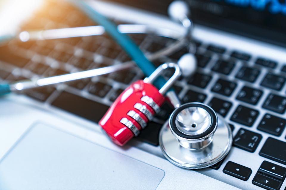 Photo of a laptop keyboard with a stethoscope and a red padlock above. Healthcare cybersecurity concept.