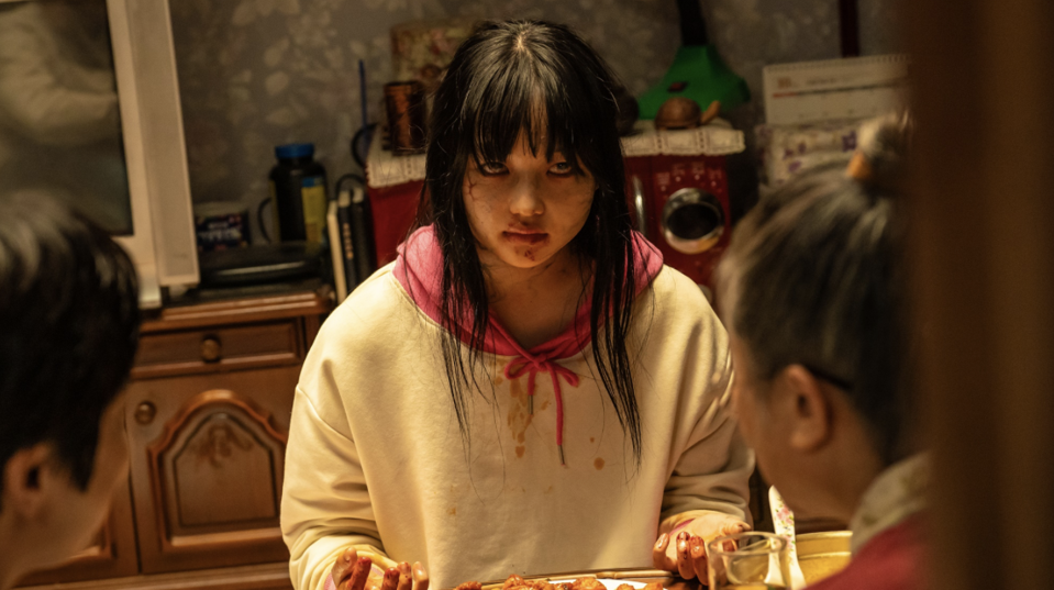 A teenage girl zombie sitting down to eat a human meal.