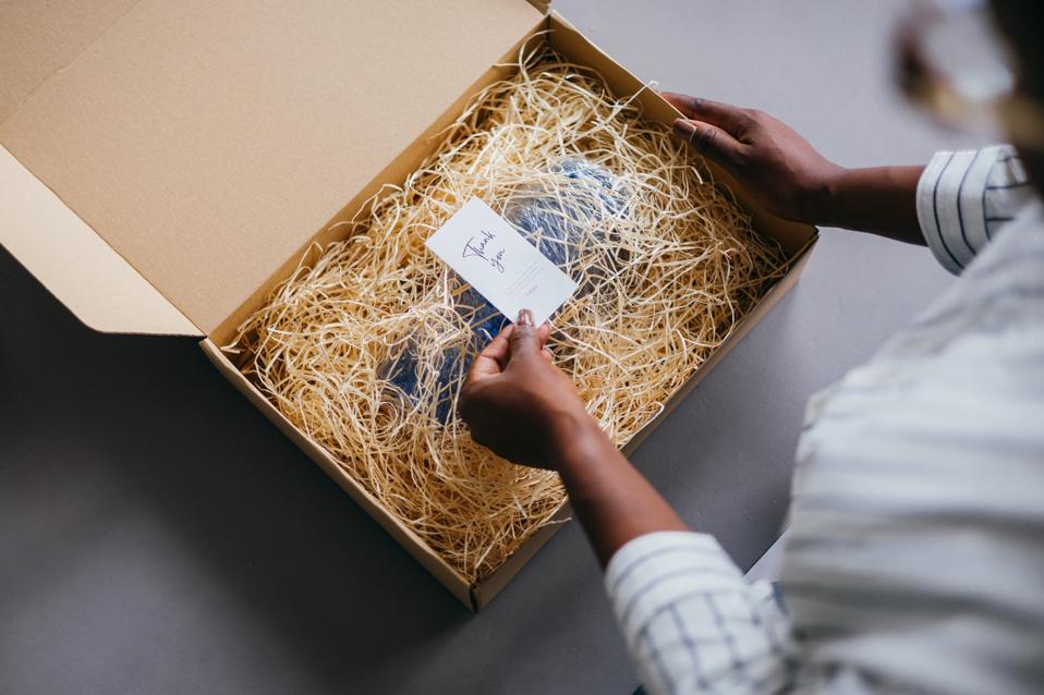 Woman opening a small box with a thank-you note and an item inside of it, covered by straw.