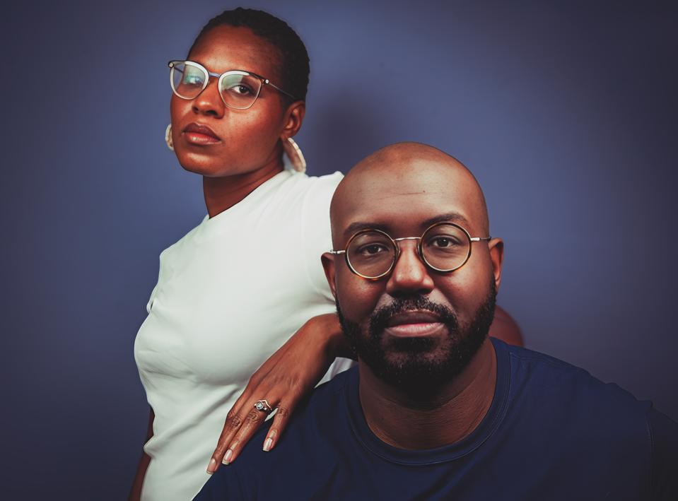 A Black man with a bald head and glasses with a Black woman with a short cut and glasses
