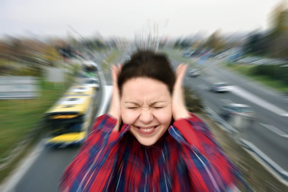 Woman covering her ears in the street while vehicles are passing by fast
