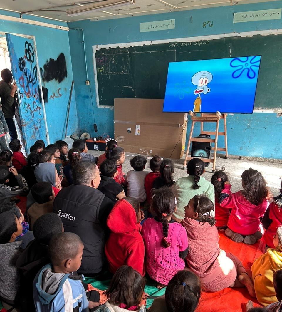 Children sit on the floor of a classroom, watching Squidward from "SpongeBob SquarePants"